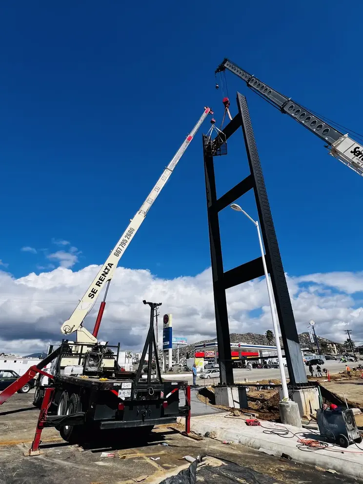 Torre negra levantándose con dos grúas contra cielo azul